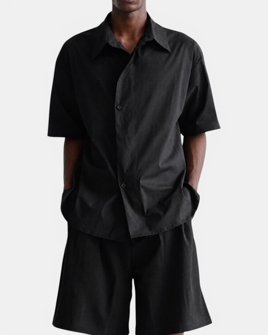 Nameless black short-sleeved cotton shirt with pointed collar and slanted placket, worn by a man.