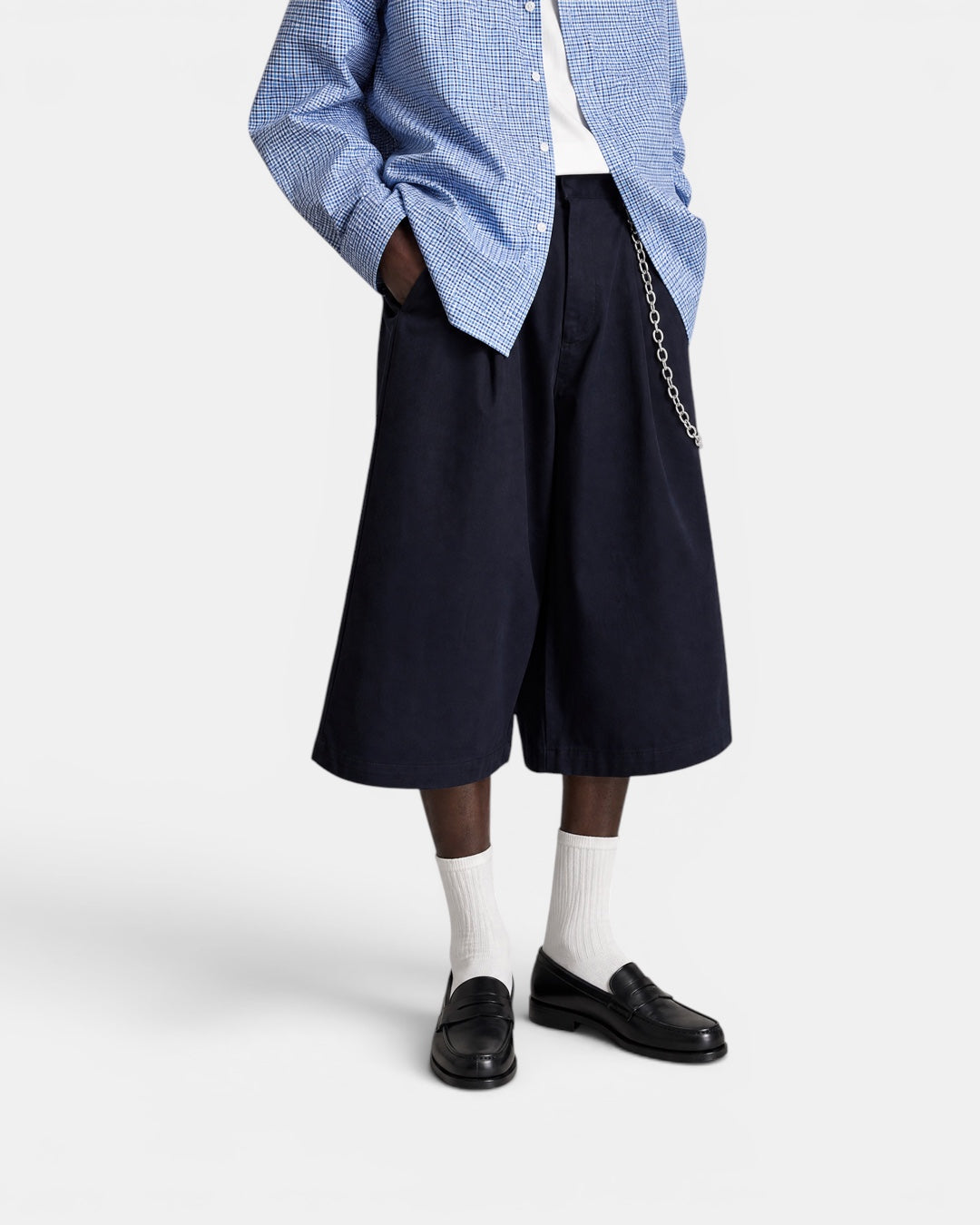 Nameless navy blue tailored wide-leg shorts with a silver chain detail. Model wears white socks and black loafers.