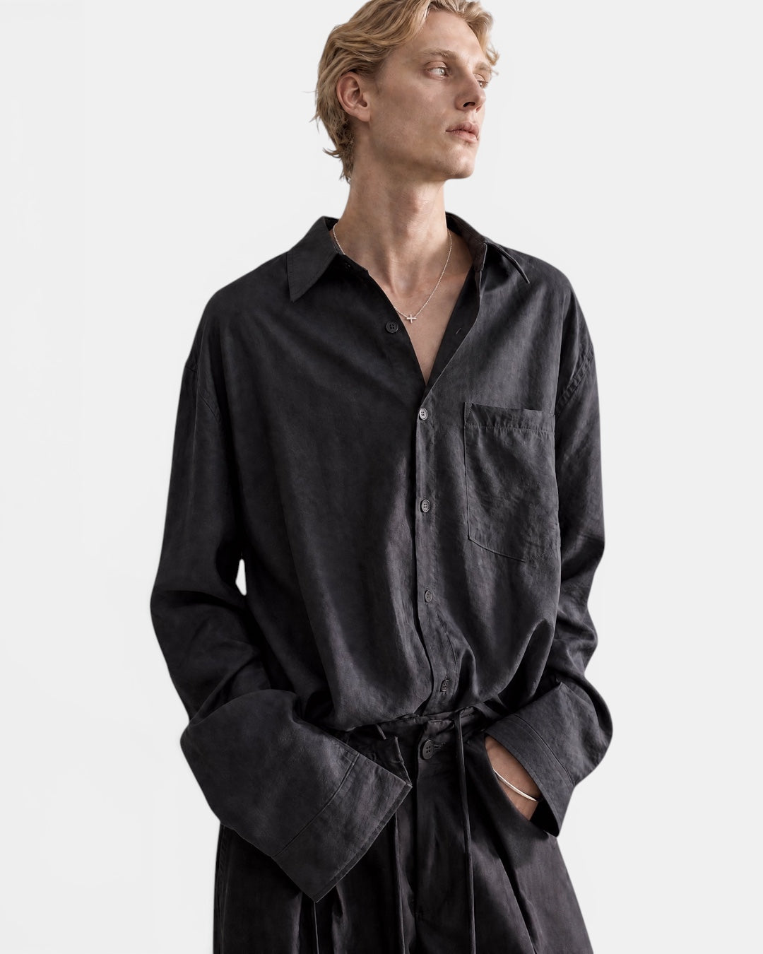 NAMELESS dark grey textured long sleeve oversized shirt with a button-up front and chest pocket. Model wears it with matching trousers.