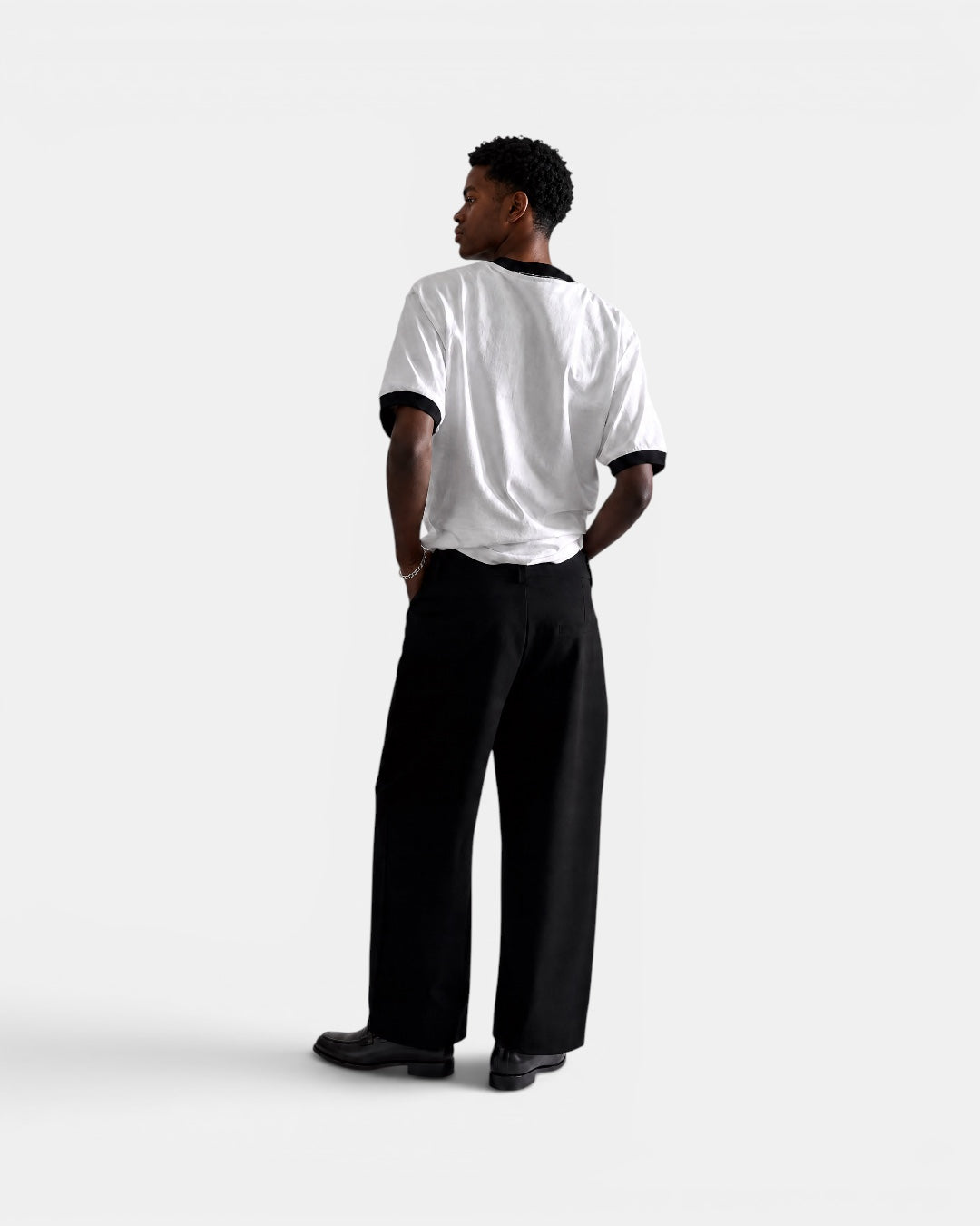 Nameless white cotton t-shirt with black trim on collar and sleeves, worn by a man in black trousers.