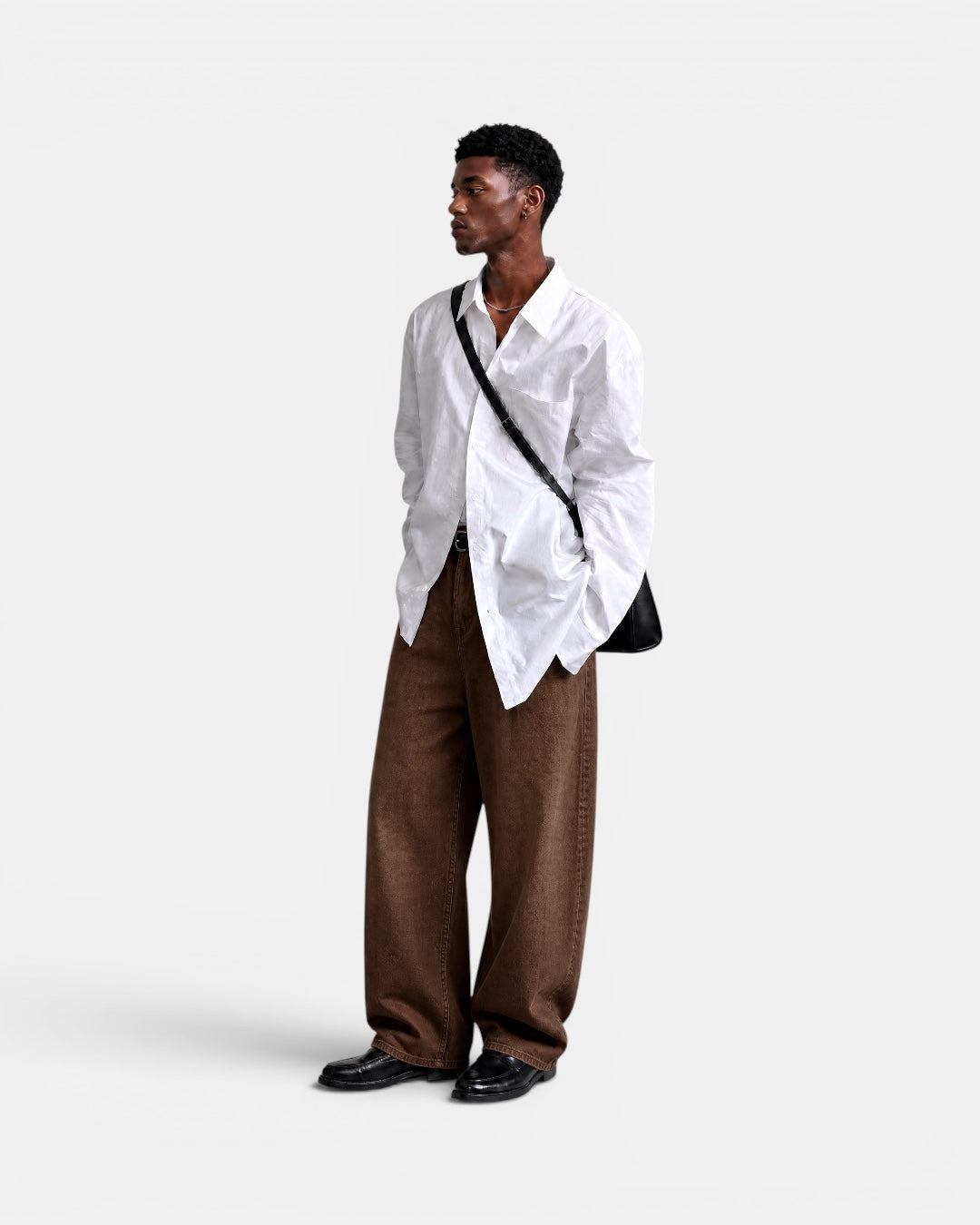 Nameless white loose-fit long-sleeved cotton shirt worn by a man with brown wide-leg jeans and black loafers.